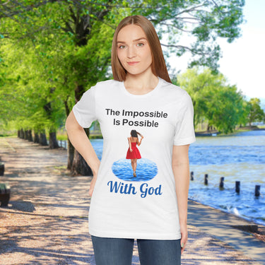 Soft, breathable Bella+Canvas t-shirt made from preshrunk cotton with “Impossible Woman” design message, “The Impossible Is Possible with God,” inspirational shirt encouraging bold obedience and faith-filled movement with God, woman in white t-shirt on waterside walkway